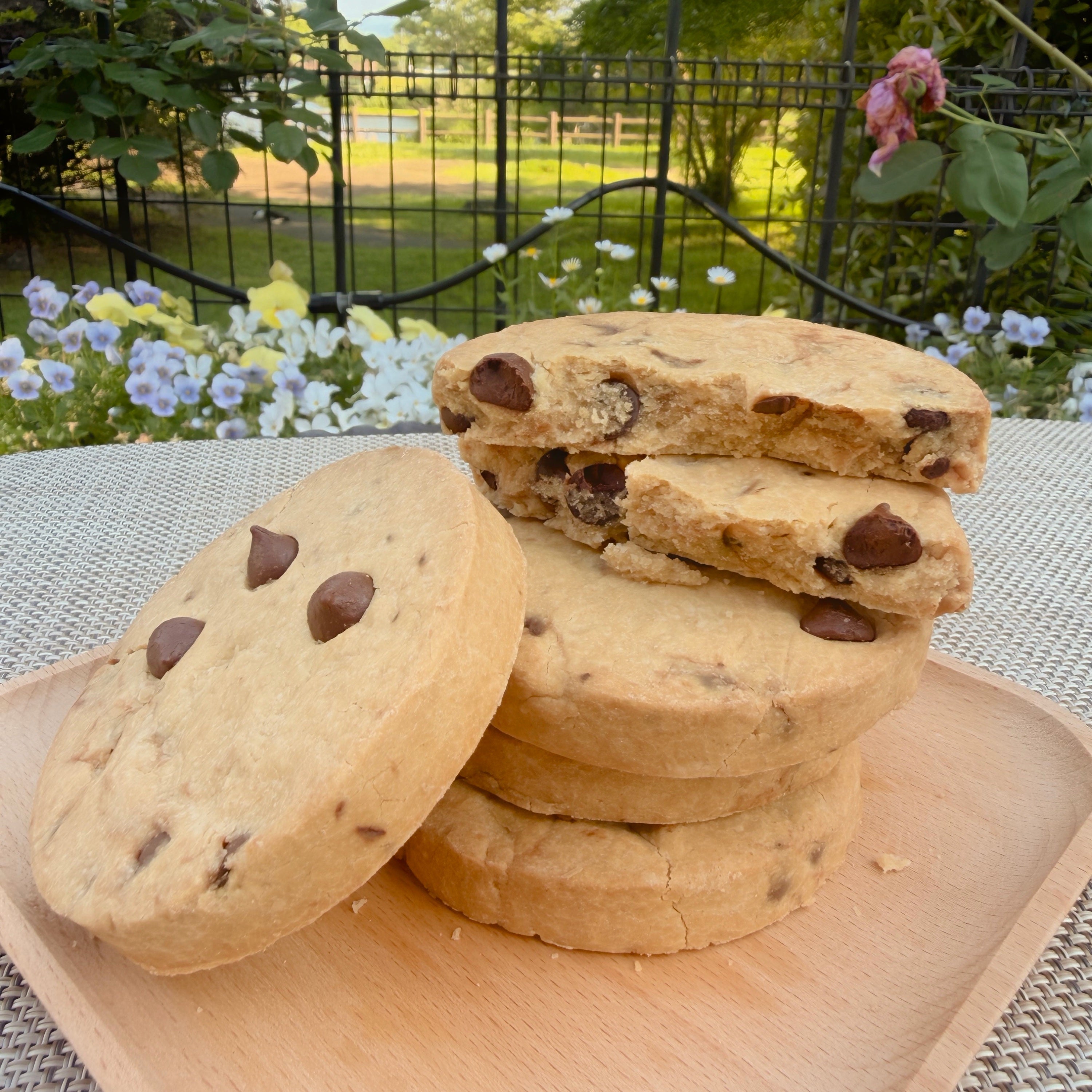 Stack of chocolate chip cookies on a wooden board with a garden background