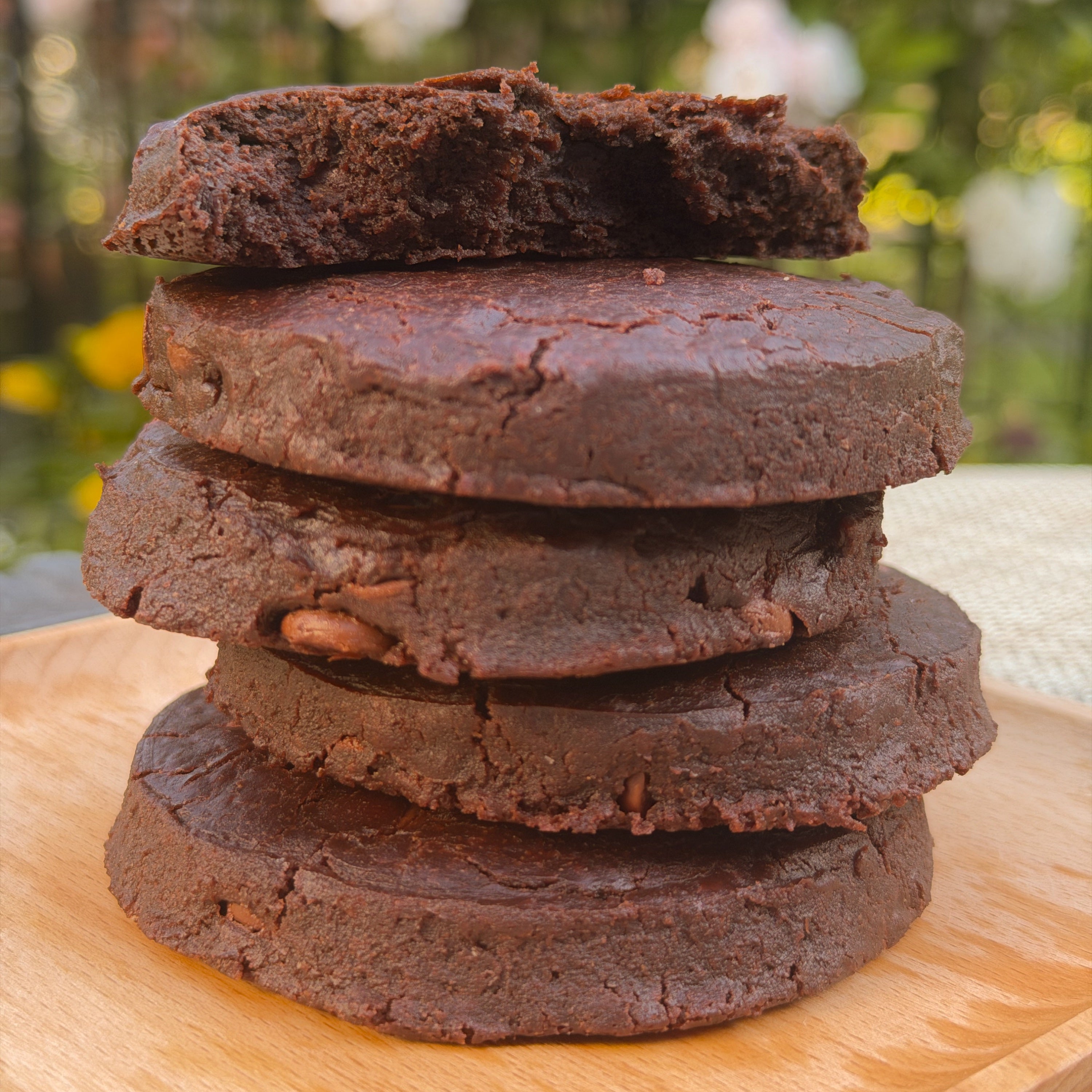 Stack of brownie cookies on a wooden surface with a blurred natural background
