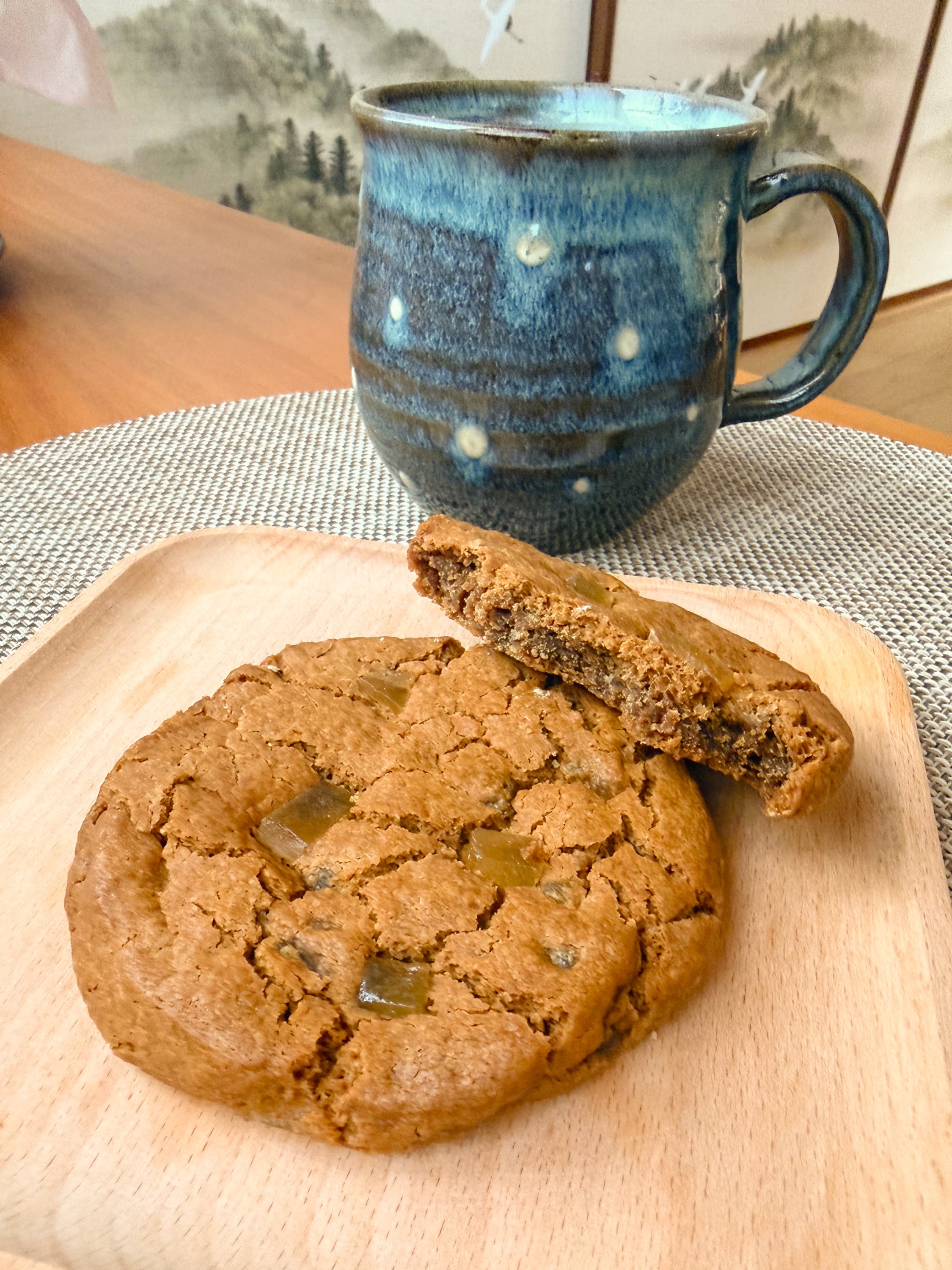 Two cookies on a wooden board with a blue ceramic mug in the background.